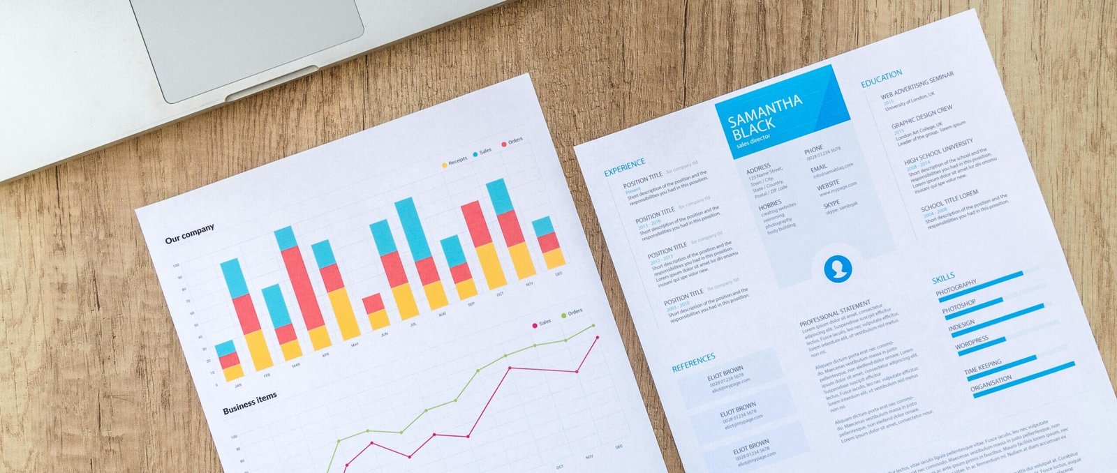 Top view of a laptop, charts, and resume on a wooden desk, showcasing business analysis and job application.